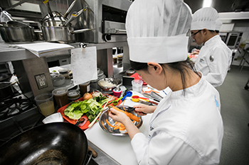 A young culinary student in chef whites plating a dish.