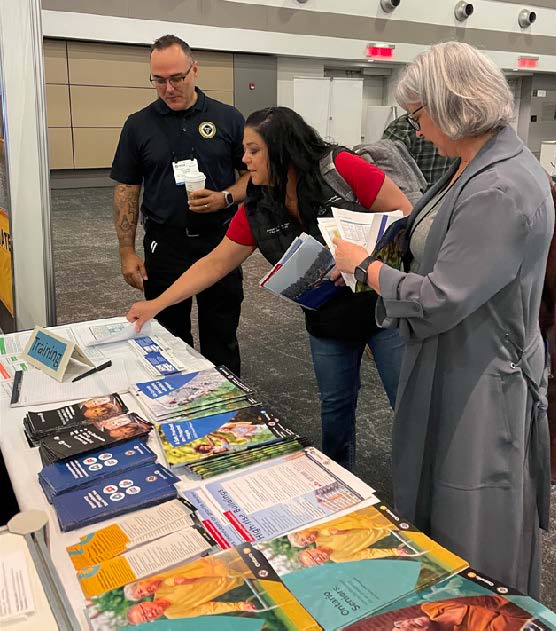 Three people standing next to a table and looking at brochures
