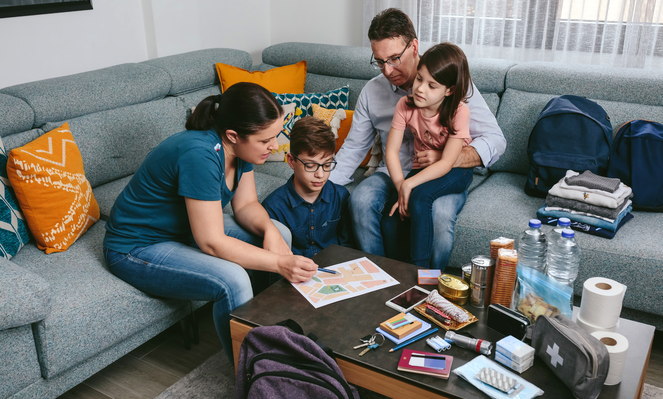 A family sitting on the couch and emergency preparedness kit items displayed on a table