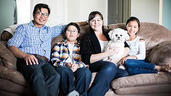 Une famille de 4 personnes assises avec leur chien sur un canapé