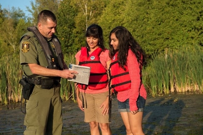 Image of conservation officer showing Fishing Regulations Summary to two women.