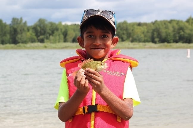 Image of boy with life jacket smiling while holding a small fish.