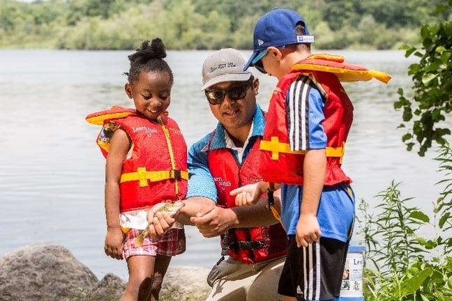 Image of a Learn to Fish instructor showing two children how to hold a small fish.