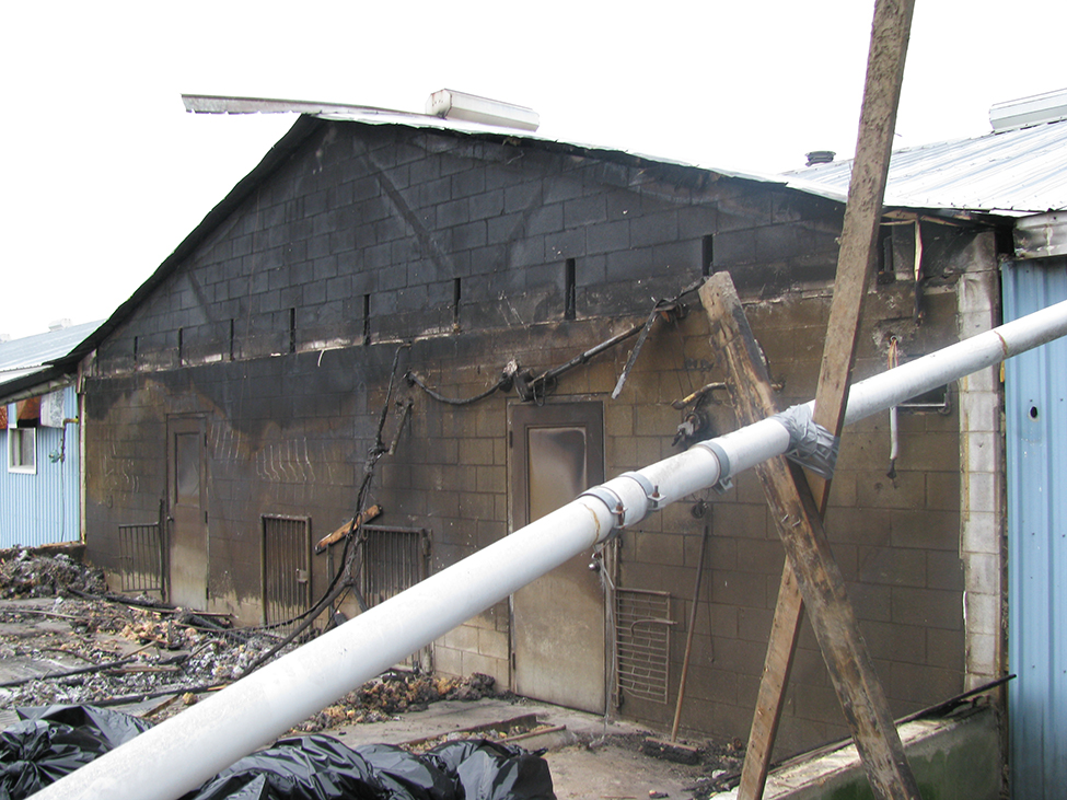 A charred concrete block wall.  A portion of the building has been destroyed in a fire, while the building on the other side of the concrete block wall remains standing.