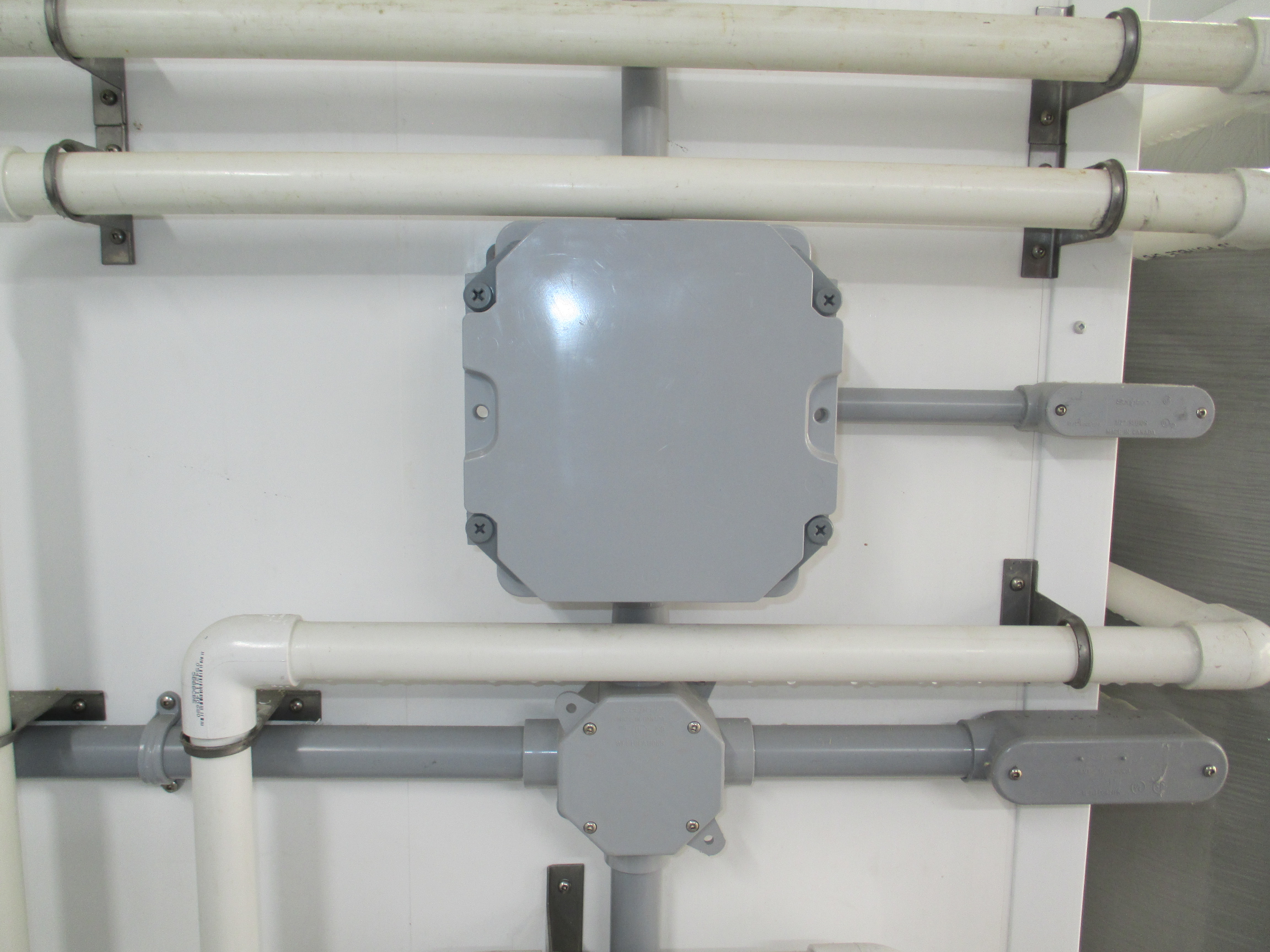 This is a photograph of a NEMA4X rated electrical enclosure mounted the wall of a barn. The enclosure is made out of grey plastic. There are no holes or vents in the enclosure that would allow moisture or corrosive gases to enter. The electrical wiring entering the enclosure is all housed in plastic conduit.