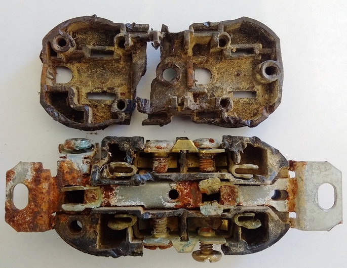 Prise électrique standard utilisée dans une étable laitière. La prise, séparée en deux, laisse voir la corrosion avancée des composants internes en cuivre.