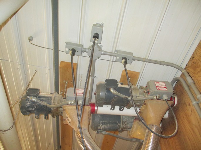 This is a photograph of three electrical motors mounted off the ceiling in a dairy barn. The three motors are all totally enclosed frames with integral cooling fans. Electrical power is supplied to motors through a common 220V plug inserted into a receptacle mounted on the ceiling. The receptacle is installed in a sealed plastic enclosure. The wiring supplying power to the receptacle is all installed in sealed plastic conduit.
