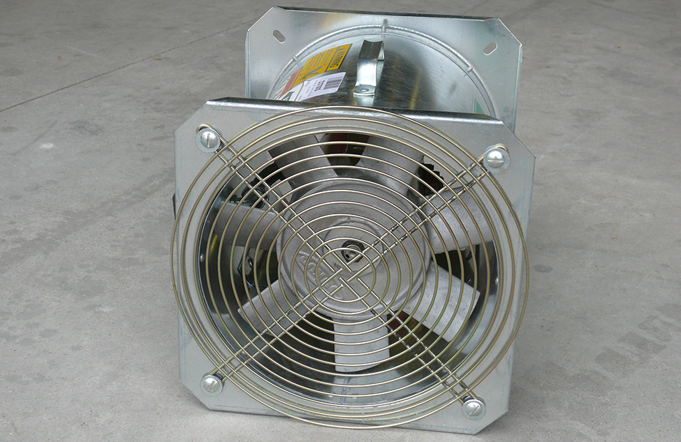 Photographie des pales d’un ventilateur axial. Le ventilateur propulse de l’air au-dessus du moteur électrique pour rafraîchir l’air. Le ventilateur et le moteur sont assemblés dans un boîtier métallique tubulaire.