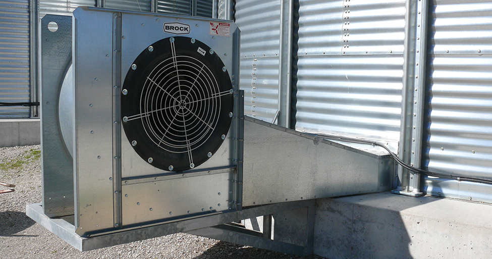 A galvanized low-speed centrifugal fan mounted at the side of a grain bin. The fan inlet is a circular screened inlet on the side of the fan housing. These fans operate at 1,750 RPM.
