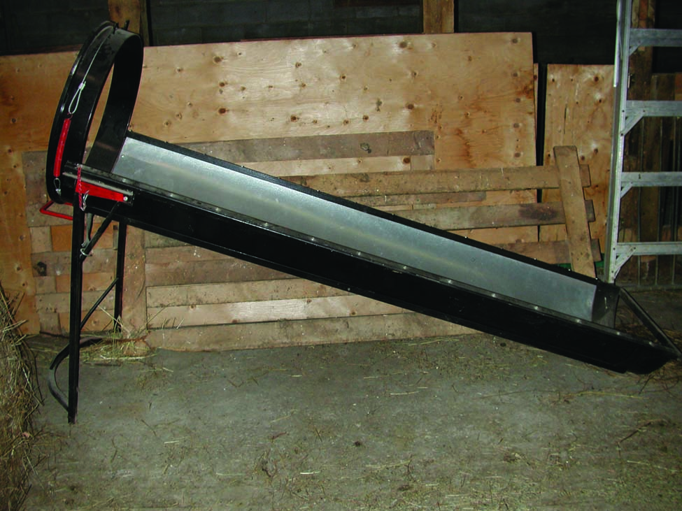 Photo of a gravity-enabled manual wool packer that consists of a long metal trough with a circular metal ring on the left side for attaching a bag. The left side is elevated.