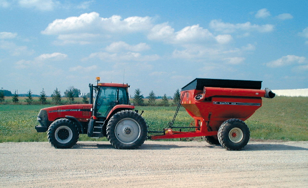 A tractor pulling a grain wagon in front of a field 