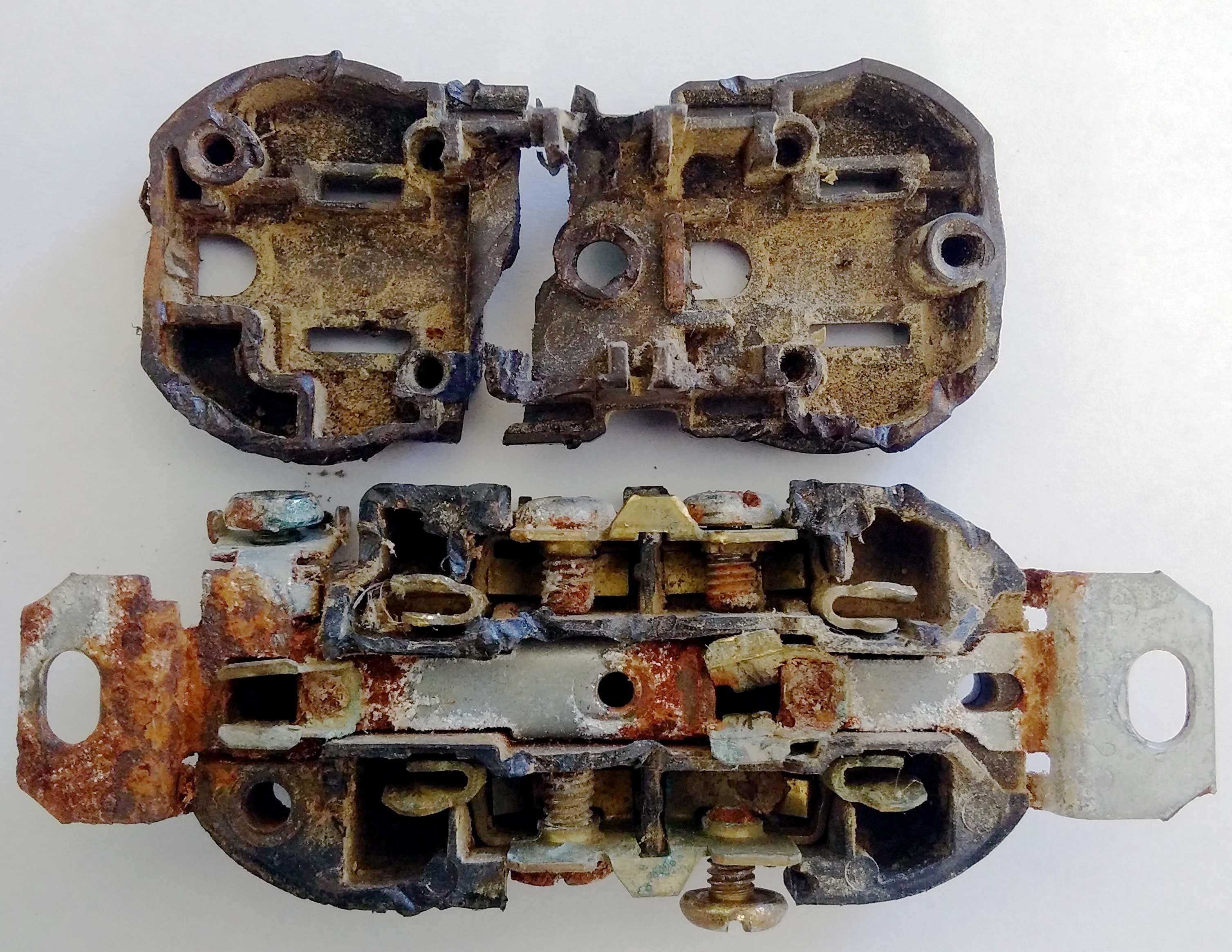 Prise électrique standard utilisée dans une étable laitière. La prise, séparée en deux, laisse voir la corrosion avancée des composants internes en cuivre