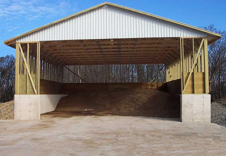 A covered, solid manure storage structure with a concrete floor and side walls. Manure is stored and kept dry inside the structure.