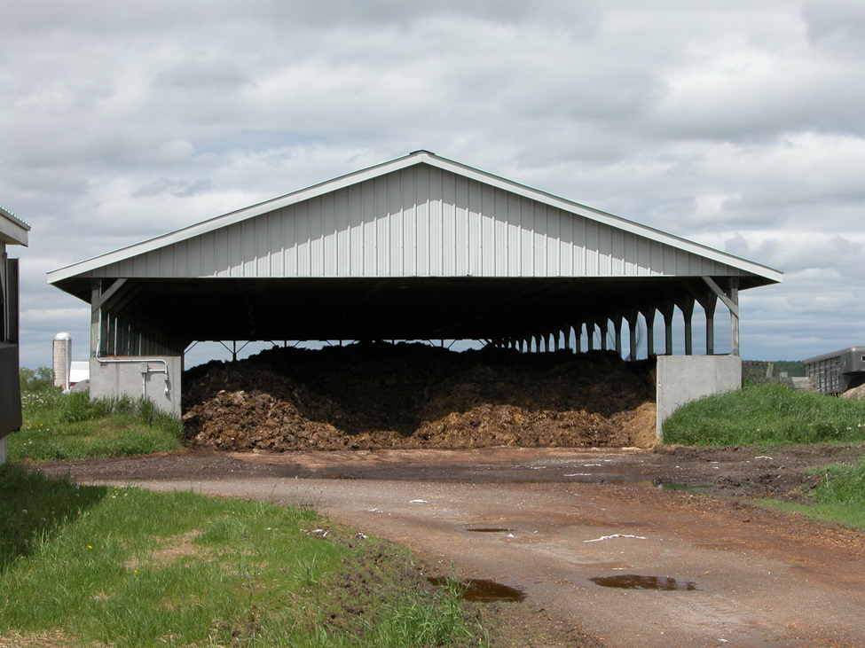 Covered, solid manure storage structure with a concrete floor and side walls. Manure is stored and kept dry inside the structure.