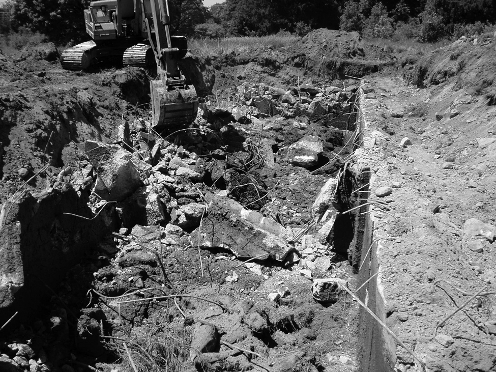 Cette photo montre une excavatrice utilisée pour démolir une structure d’entreposage de fumier en béton. Les matériaux de construction sont enfouis sur place.
