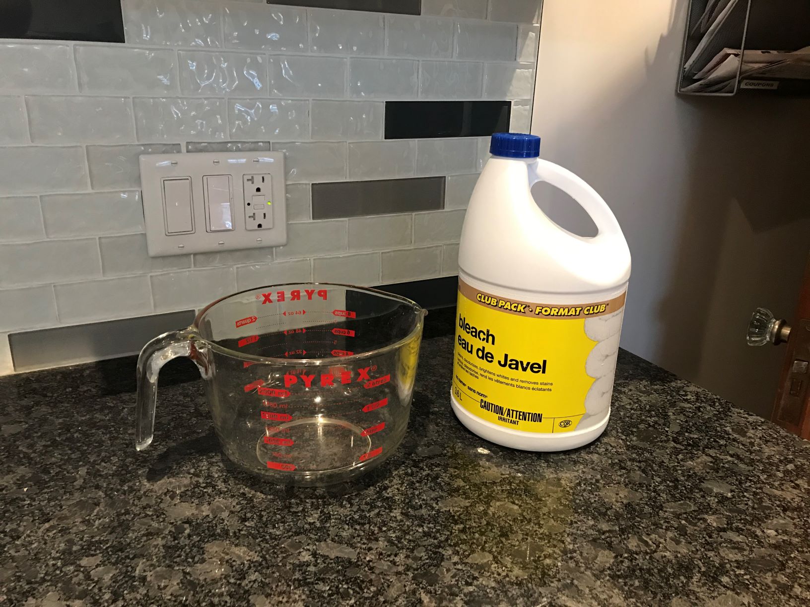 A glass measuring cup and a bottle of bleach sitting on a countertop.