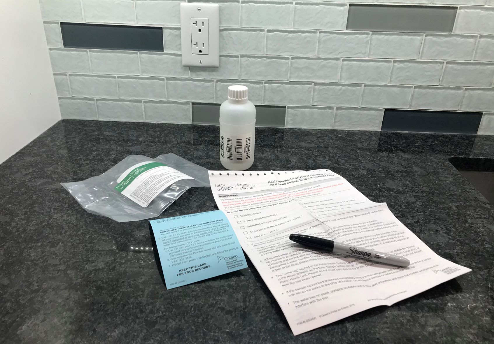 A typical private water well sample kit – sample bottle, a form and instruction paper and a pen - on a countertop