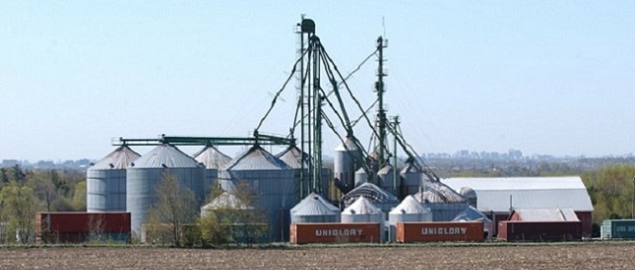 A photo of grain elevators on a farm with railway cars in front of the grain elevators. In the distance are high rise buildings.
