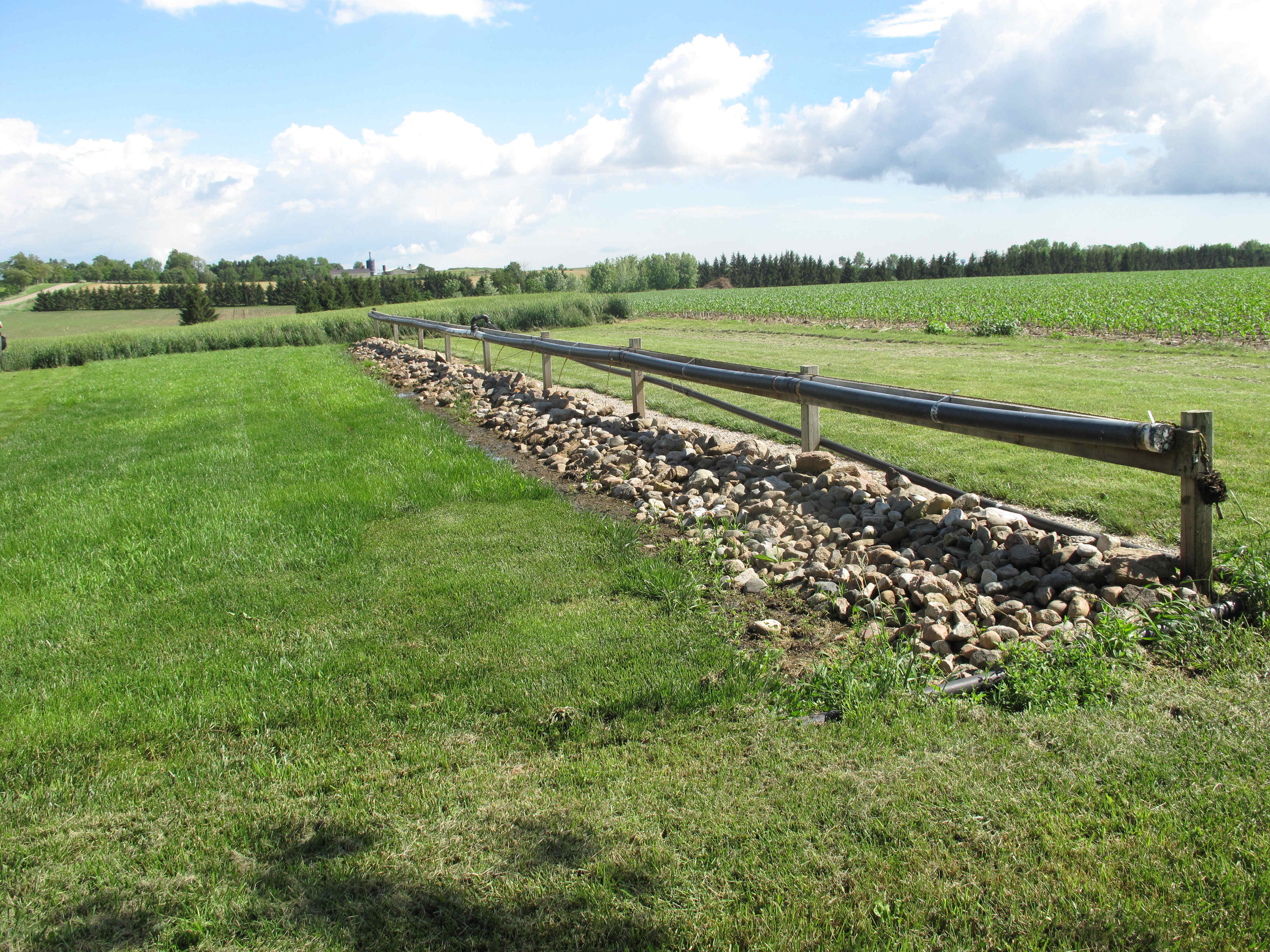 Length of a vegetated filter pipe that sits above the ground on wood supports in a field; the ground immediately below the pipe is covered with gravel to enhance drainage
