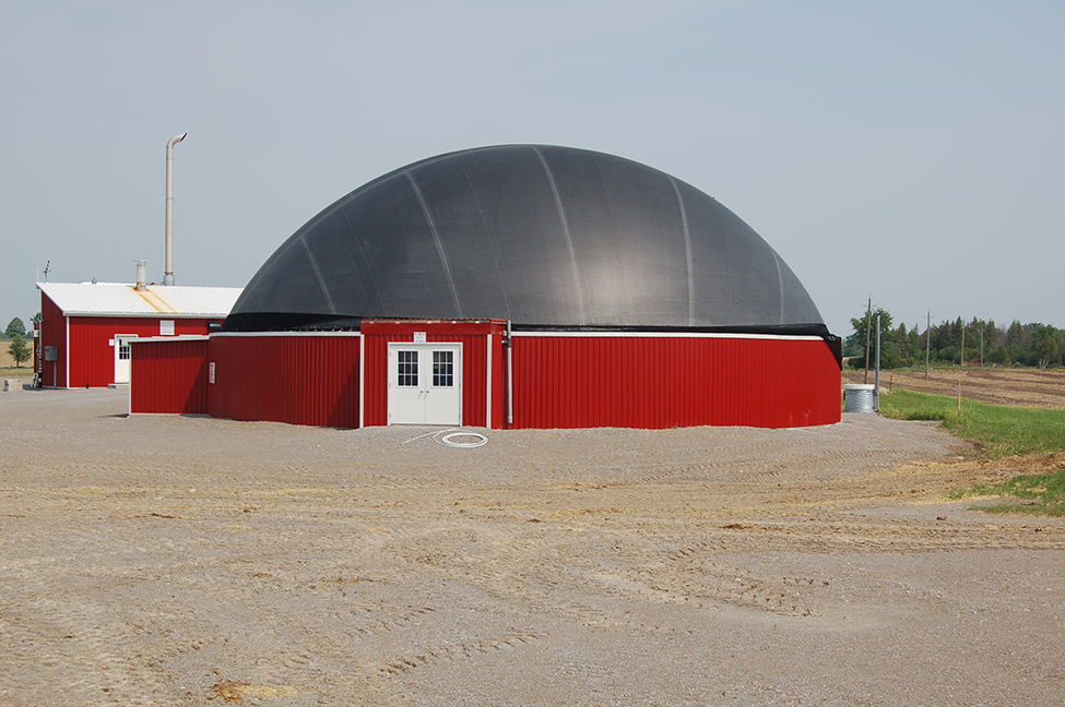 Photo d’un réservoir circulaire en béton avec des parements d’aluminium, recouvert d’un dôme noir gonflé sur une surface en gravier.