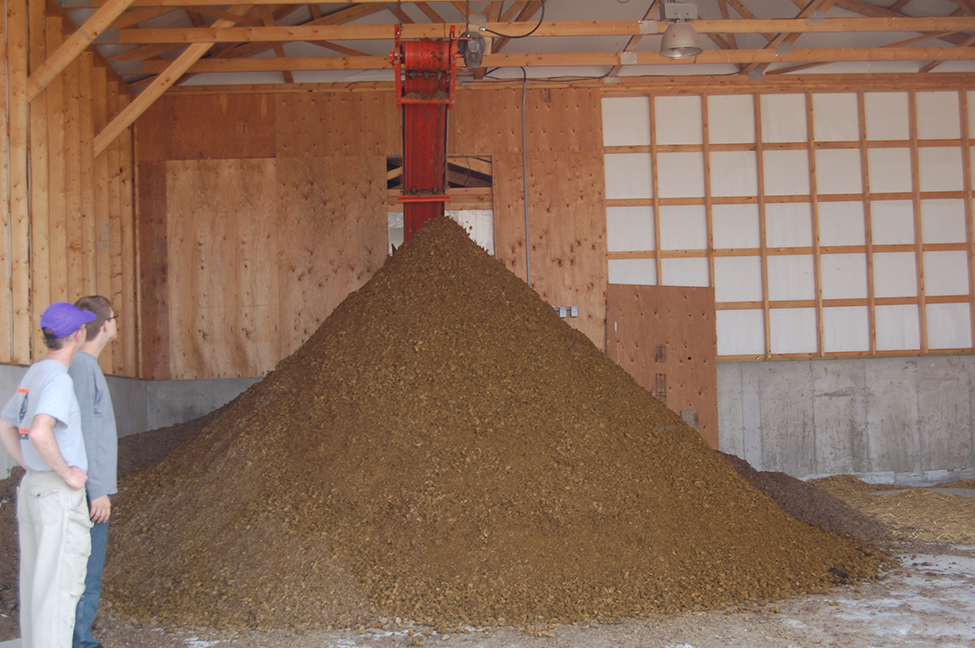 Photo d’un tas de digestat solide en forme de pyramide en dessous d’un séparateur avec presse à vis dans un hangar.