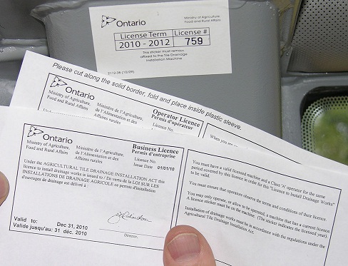 This photo shows a contractor holding his Business and Operator licences issued by OMAFRA under the Agricultural Tile Drainage Installation Act.