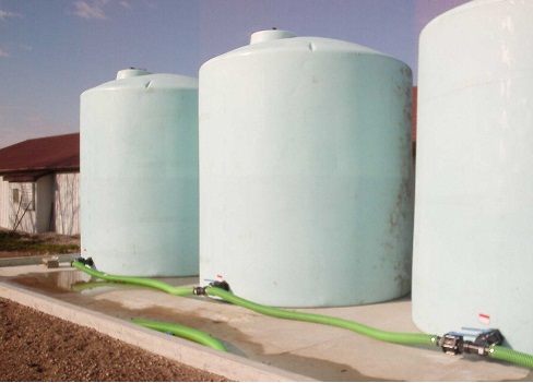 Photo d’une exploitation agricole montrant trois grands réservoirs de stockage en polyéthylène placés sur une dalle de béton qui est entourée d’un muret de rétention (30 centimètres de haut).