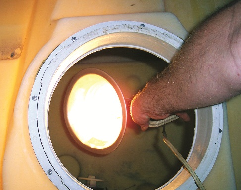 Photo showing how to candle a polyethylene storage tank by holding a bright light inside the tank and checking the outside surface of the tank for crazing and cracks.