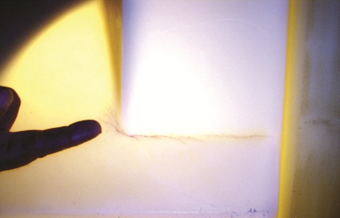 Close-up photo of polyethylene tank wall being candled from inside showing crack at junction point. 