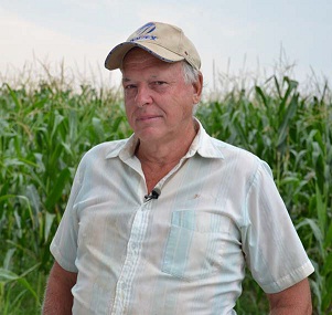 Agriculteur portant une casquette de baseball devant un champ de maïs.