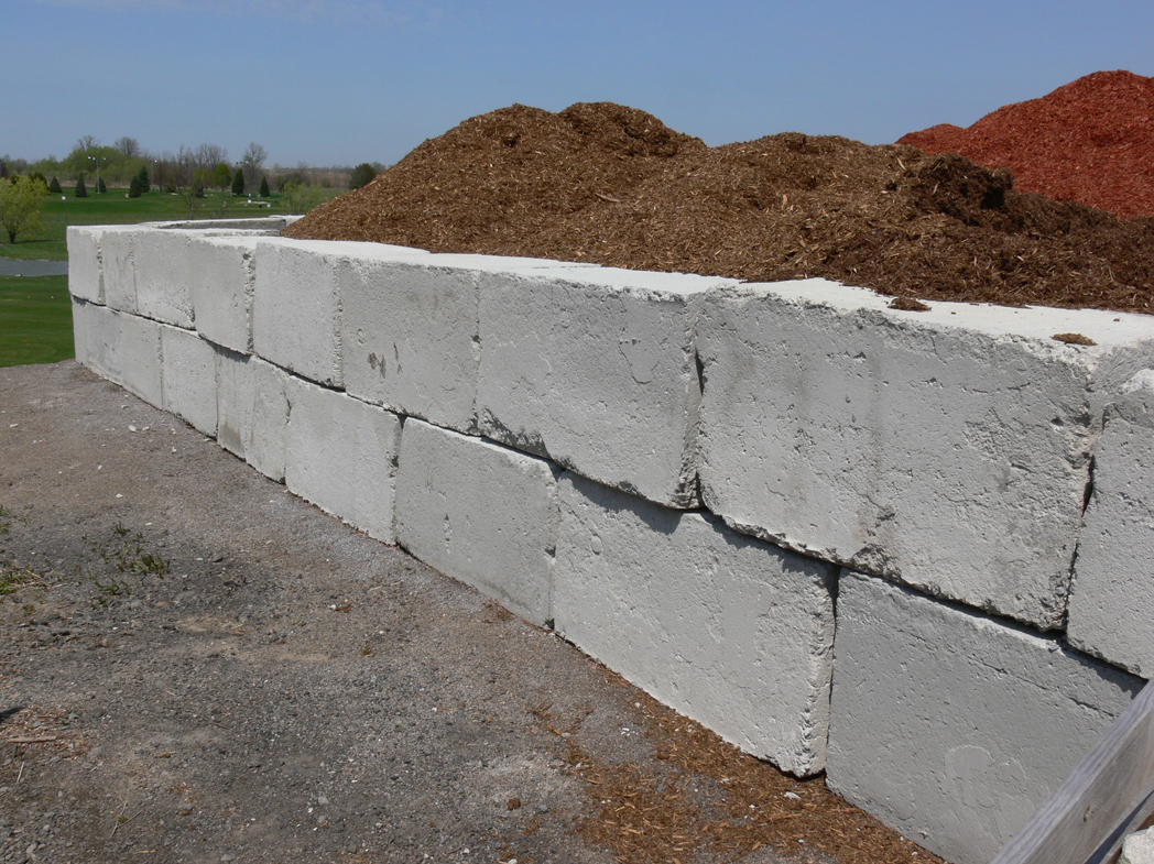 Large concrete blocks stacked two high like bricks in a wall and they are storing some reddish coloured wood chips.