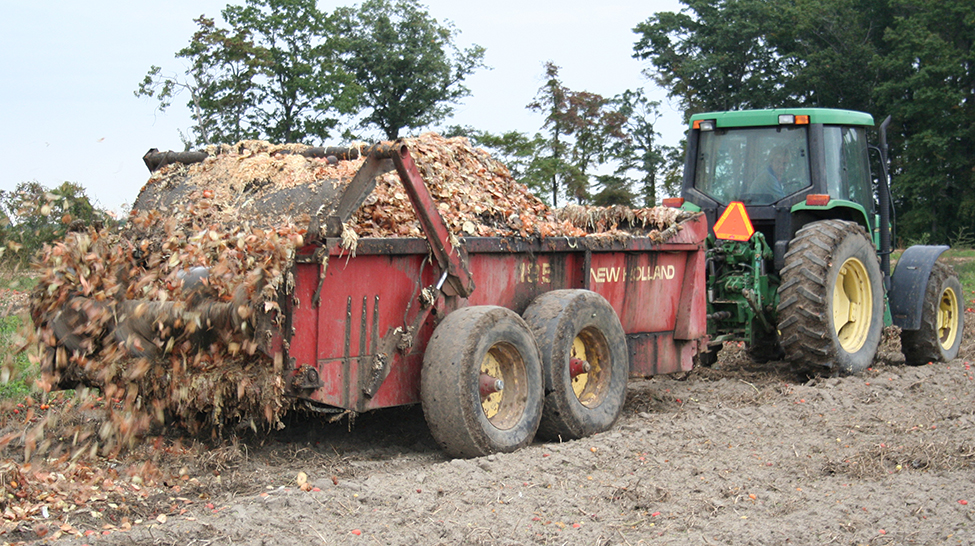 A tractor pulling a wagon in a field and land applying onion waste