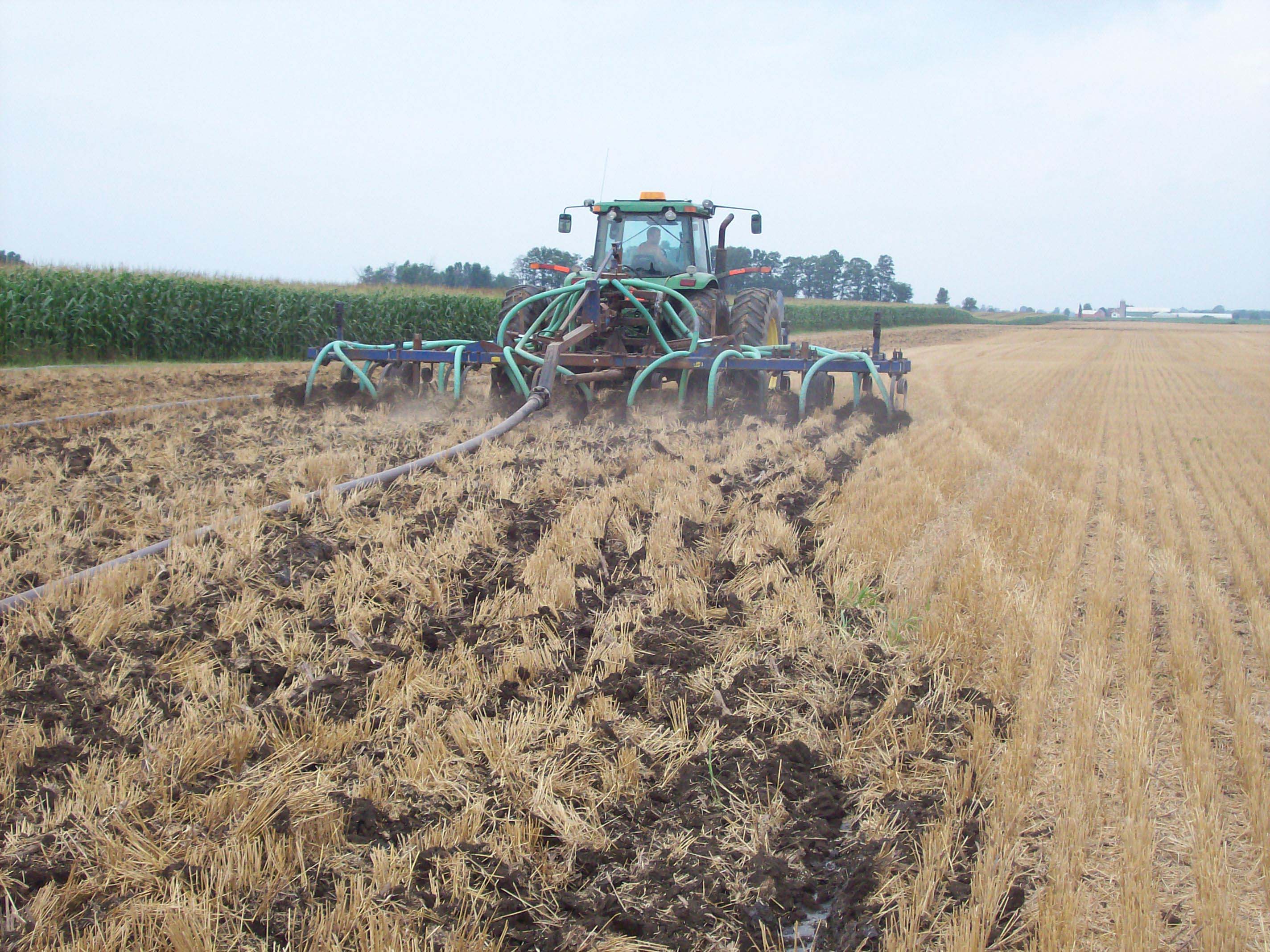 A tractor in a field applying liquid biosolids using a drag hose and injecting the nutrients into the soil