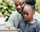 Un parent et sa fille lisent du contenu affiché sur une tablette électronique.