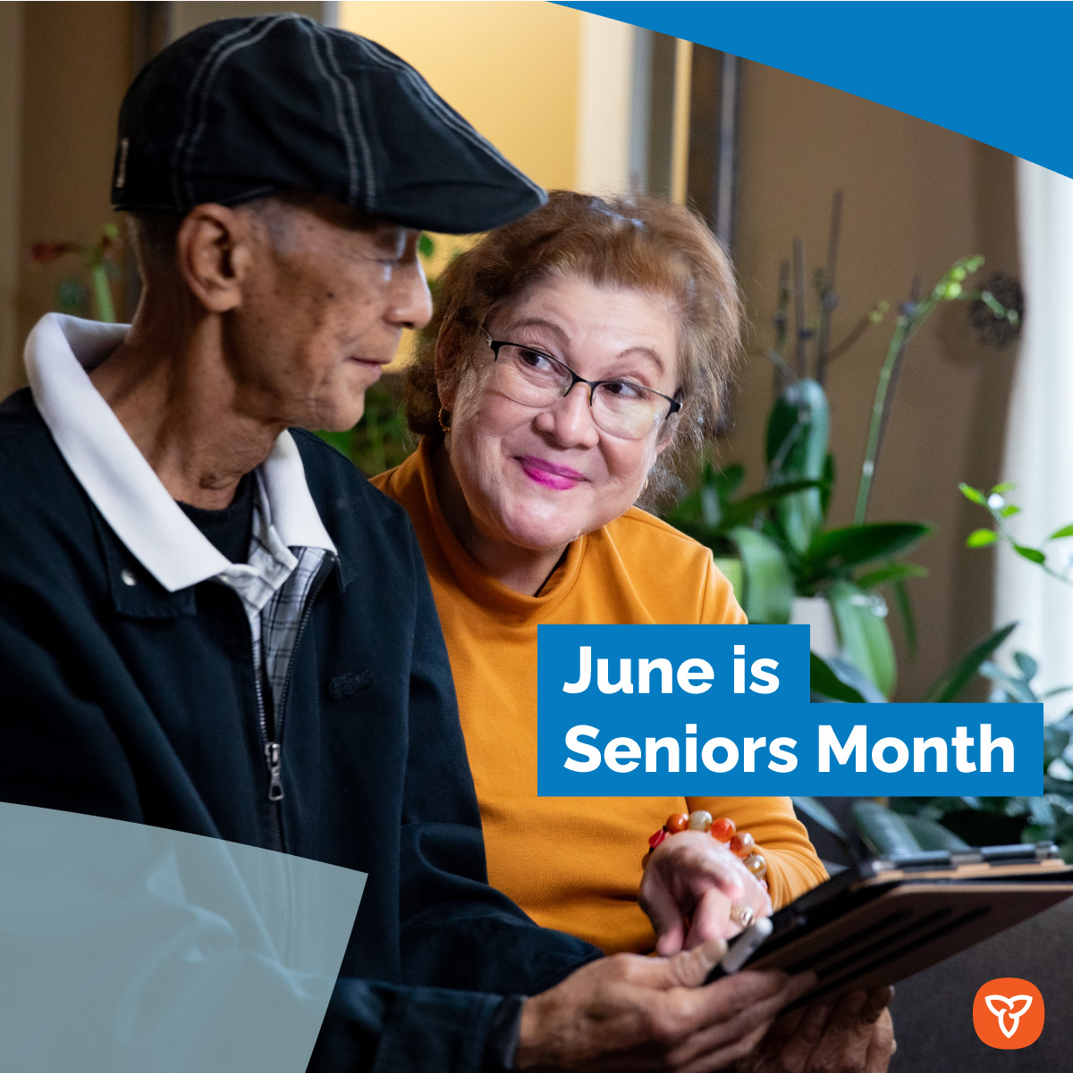 Two older adults smiling while sitting on a couch holding a tablet. Text reads: June is Seniors Month.