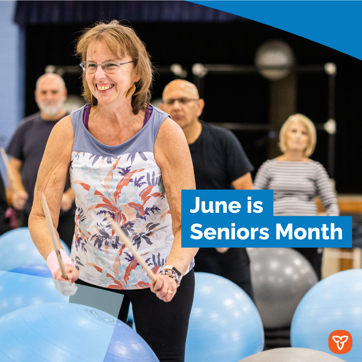 An older adult smiling while attending a drum fitness class with other older adults. Text reads: June is Seniors Month.