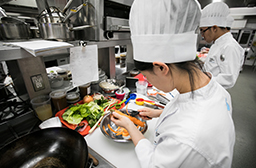 Une jeune élève vêtue de l’habit blanc des chefs s’initie à l’art culinaire.