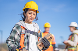 Une jeune élève portant un équipement de protection travaille sur un chantier de construction. 