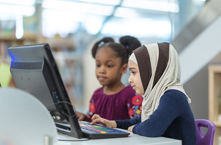 Deux élèves du primaire assises à une table qui utilisent un ordinateur pour apprendre ensemble