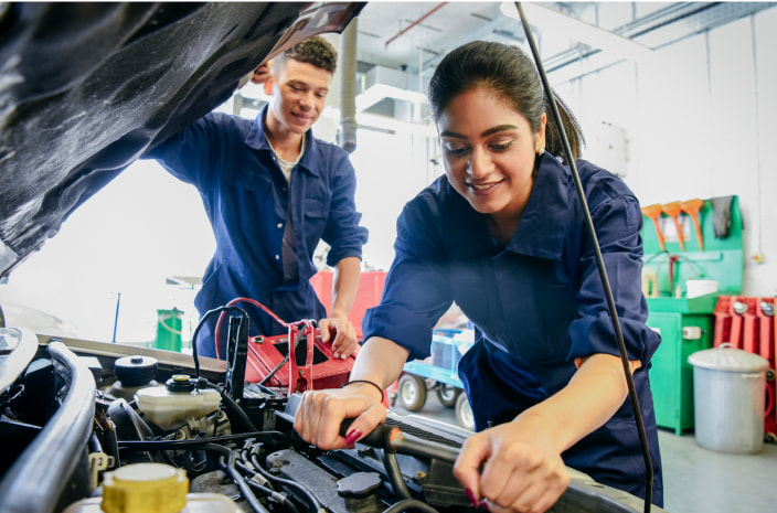 Two high school students working on a car in auto shop class