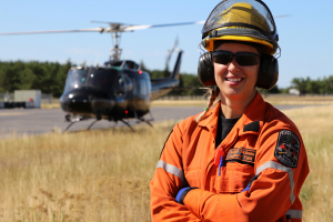 A FireRanger smiles for the camera. A black helicopter is positioned behind them.