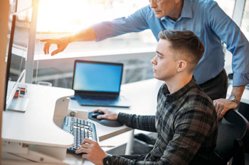 A student being shown something on an office computer by a supervisor.