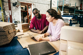 A student and supervisor looking at a tablet in a manufacturing warehouse.