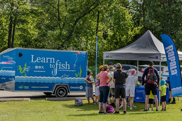 Un groupe d’individus de tous âges devant l’unité mobile du programme Apprenez à pêcher.