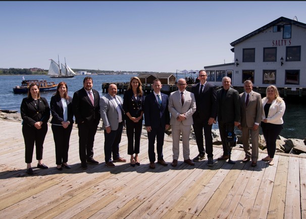Groupe de ministres fédéraux, provinciaux et territoriaux alignés sur une jetée en bois, devant un bâtiment blanc et le plan d’eau du port, lors de la réunion d’août&nbsp;du CMFC