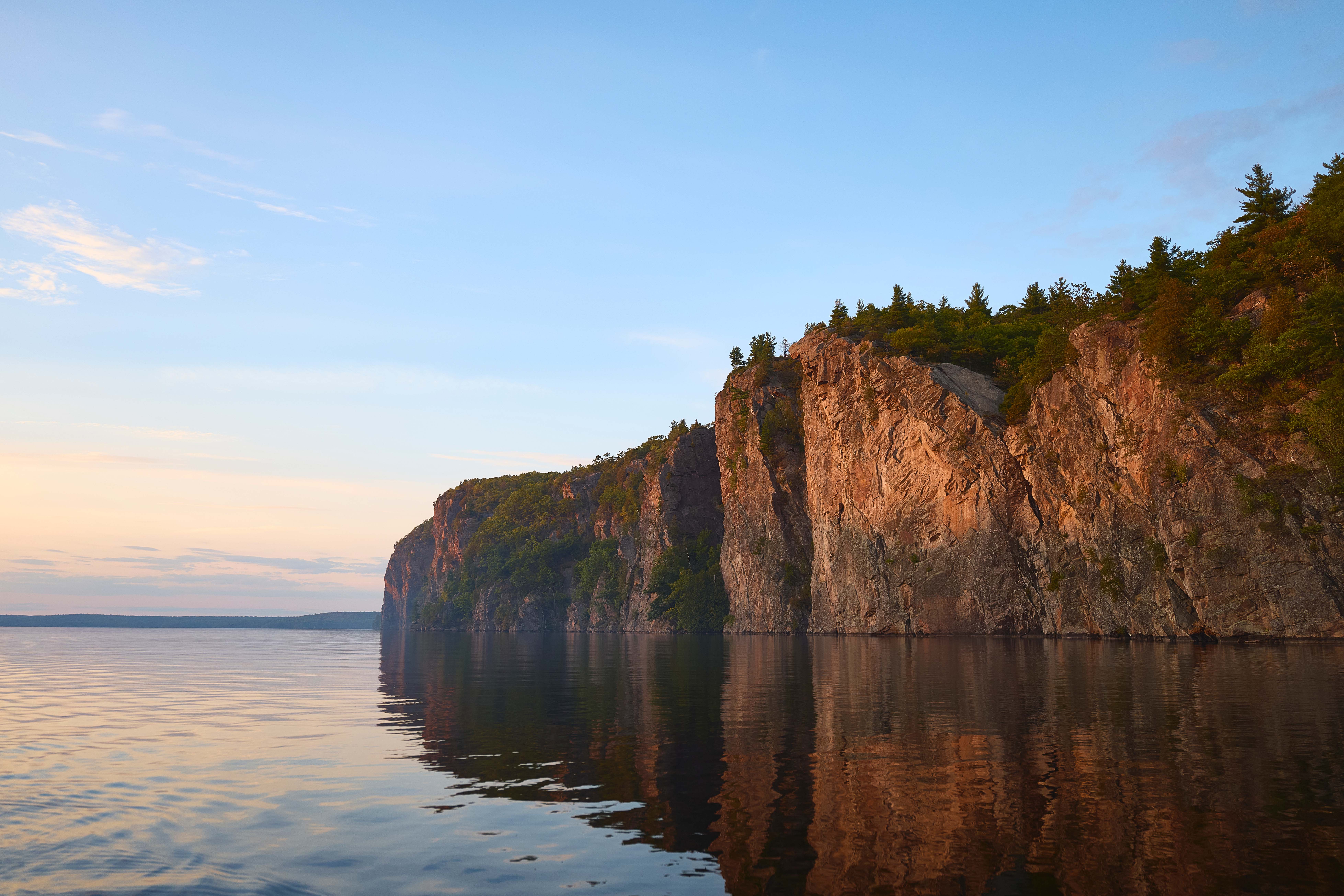 Bon Echo Provincial Park’s rocky cliff rising above a calm lake with reflections and trees along the shoreline.