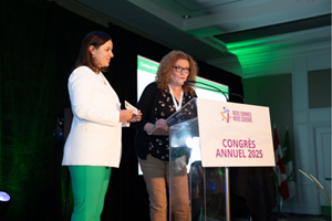 L’Honorable Natalia Kusendova‑Bashta, ministre des Soins de longue durée, remet l’identifiant visuel à Barbara Ceccarelli, directrice générale du Centre d’accueil Héritage, devant un pupitre arborant un panneau indiquant le nom du congrès annuel 2025 de l’Assemblée de la francophonie.