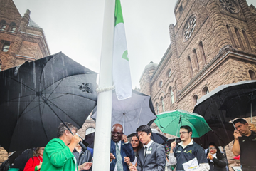 Des représentants de l'Assemblée de la francophonie et de différents partis politiques et de la communauté francophone et francophile rassemblés en plein air pour hisser le drapeau franco-ontarien lors d'une cérémonie à Queen’s Park.