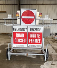 Panneau routier mobile portant les mentions « Road Closed » et « Route Fermée », surmonté d'un symbole d'interdiction de circuler.