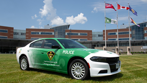 Un véhicule de la Police provinciale de l’Ontario, arborant des insignes verts à l’effigie de la francophonie ontarienne, est stationné devant un bâtiment public. Cinq drapeaux sont visibles devant le bâtiment : le drapeau franco‑ontarien, le drapeau de l’Ontario, celui du Canada, le drapeau de la Police provinciale de l’Ontario et le drapeau 2ELGBTQI+.